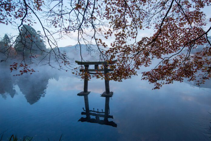 Torii gate at Kinrin Lake in Yufuin with steam rising from the lake surface on an autumn morning.